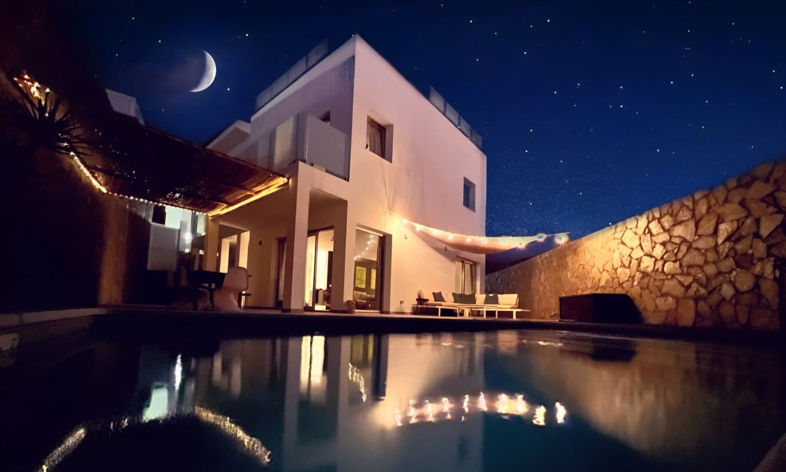 Casa Tilda lit up at night, reflected in the pool